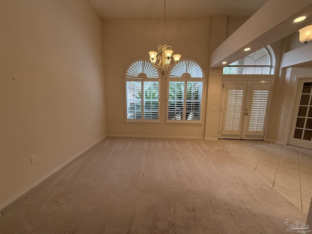 carpeted spare room featuring a chandelier, french doors, and a towering ceiling