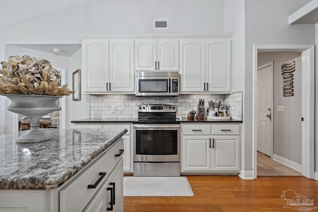 1333 Dubose Rd, Gulf Breeze, FL 32563 - kitchen with stainless steel appliances, decorative backsplash, light wood-style flooring, white cabinetry, and dark stone countertops