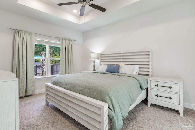 carpeted bedroom with ceiling fan and a tray ceiling