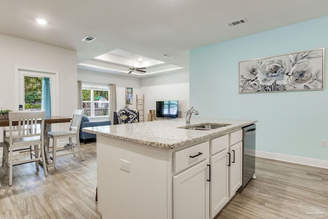 kitchen with stainless steel dishwasher, a raised ceiling, sink, a center island with sink, and white cabinetry