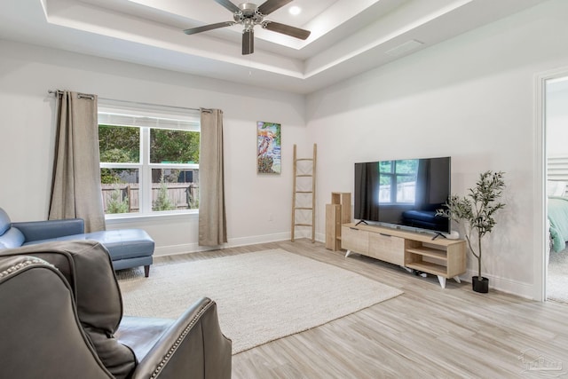 living room featuring light hardwood / wood-style floors, a raised ceiling, and ceiling fan