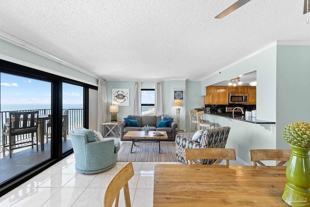 tiled living room featuring ceiling fan, a textured ceiling, crown molding, and a water view