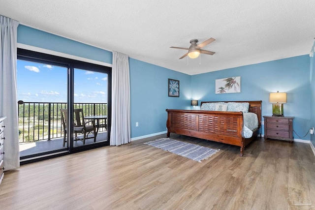 bedroom with access to exterior, a textured ceiling, multiple windows, and hardwood / wood-style floors