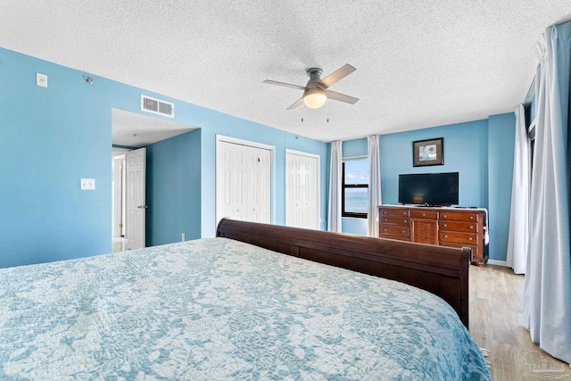 bedroom featuring a textured ceiling, ceiling fan, two closets, and light hardwood / wood-style floors