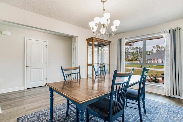 dining area with wood-type flooring, a textured ceiling, and an inviting chandelier