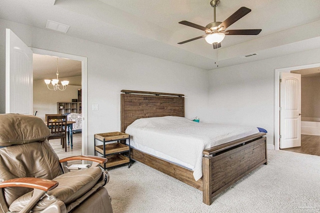 carpeted bedroom with ensuite bathroom, ceiling fan with notable chandelier, and a tray ceiling