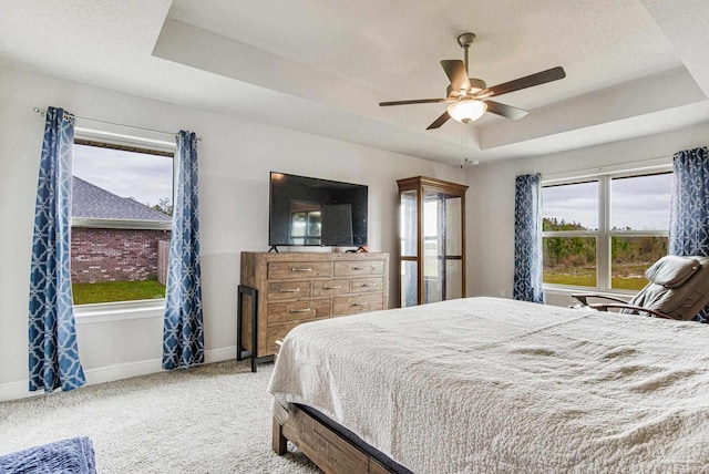 carpeted bedroom with ceiling fan and a tray ceiling