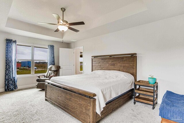 bedroom featuring a raised ceiling, light colored carpet, and ceiling fan