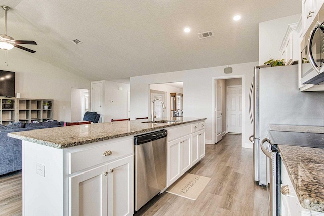 kitchen featuring an island with sink, lofted ceiling, sink, white cabinetry, and stainless steel appliances