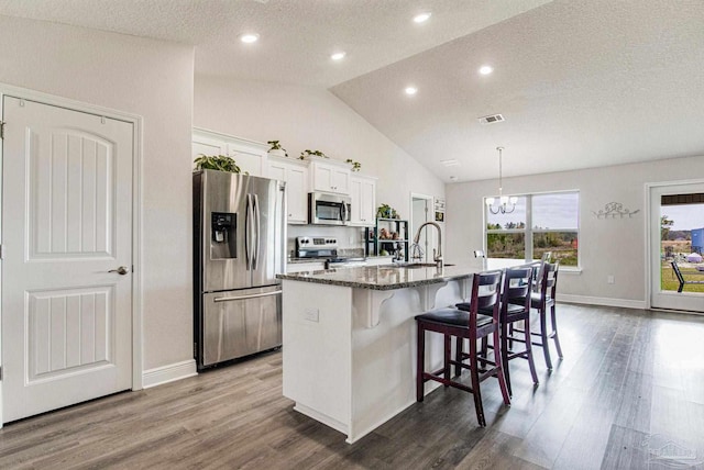 kitchen with a breakfast bar, appliances with stainless steel finishes, an island with sink, white cabinets, and dark stone counters