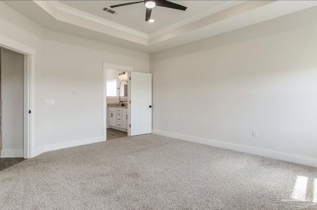 unfurnished bedroom featuring visible vents, baseboards, a sink, a tray ceiling, and dark colored carpet