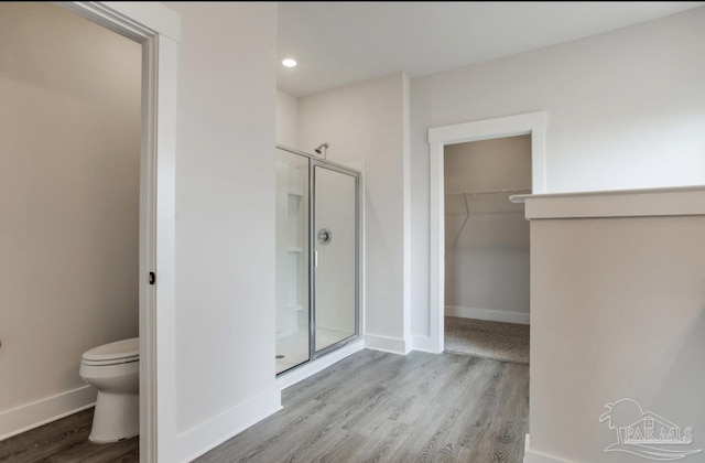 bathroom featuring baseboards, wood finished floors, toilet, and a shower stall