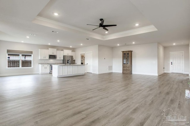 unfurnished living room featuring a ceiling fan, a raised ceiling, light wood-style flooring, baseboards, and recessed lighting