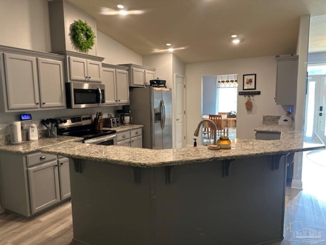 kitchen with gray cabinetry, light stone countertops, stainless steel appliances, and a breakfast bar area