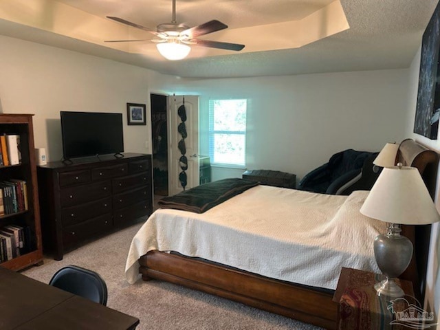 bedroom with a raised ceiling, ceiling fan, and light colored carpet