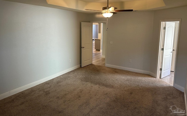 carpeted spare room with a raised ceiling and ceiling fan