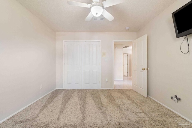 unfurnished bedroom with ceiling fan, a closet, light carpet, and a textured ceiling