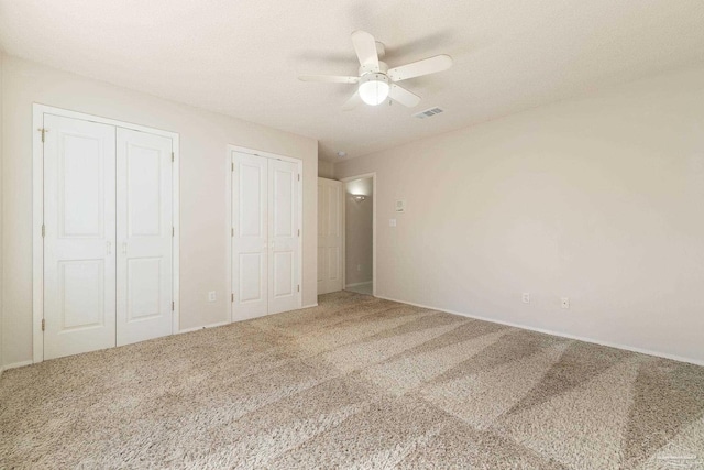 unfurnished bedroom featuring ceiling fan, carpet floors, and two closets