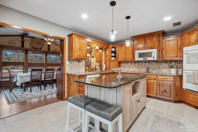 kitchen with white appliances, a kitchen bar, dark stone countertops, a sink, and a center island