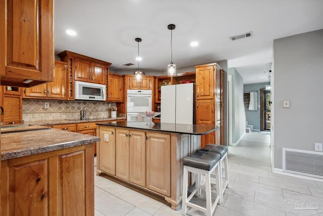 kitchen with a sink, visible vents, a kitchen island, and white appliances