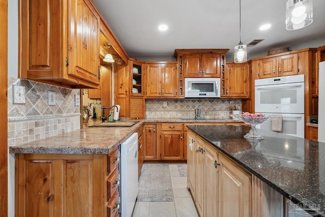 kitchen featuring white appliances, dark stone counters, backsplash, a sink, and visible vents