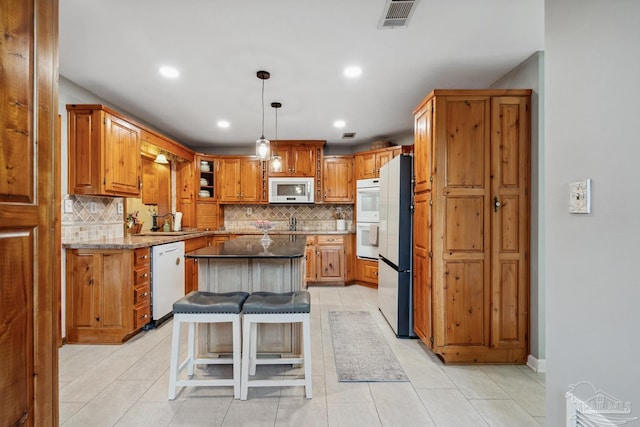 kitchen with stone counters, a center island, brown cabinets, white appliances, and visible vents