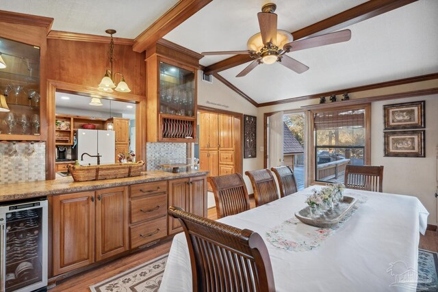 dining space with crown molding, ceiling fan, light wood-style floors, beverage cooler, and vaulted ceiling with beams