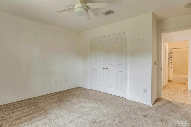 unfurnished bedroom featuring ensuite bath, ceiling fan, light colored carpet, and a closet