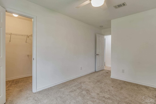 unfurnished bedroom with a closet, ceiling fan, a spacious closet, and light carpet