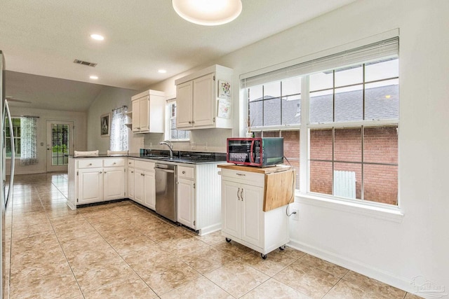 kitchen with white cabinets, dishwasher, vaulted ceiling, kitchen peninsula, and light tile patterned flooring