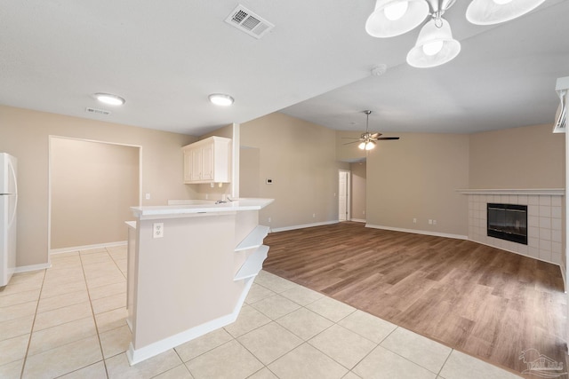 kitchen featuring kitchen peninsula, ceiling fan, a fireplace, light hardwood / wood-style floors, and white refrigerator