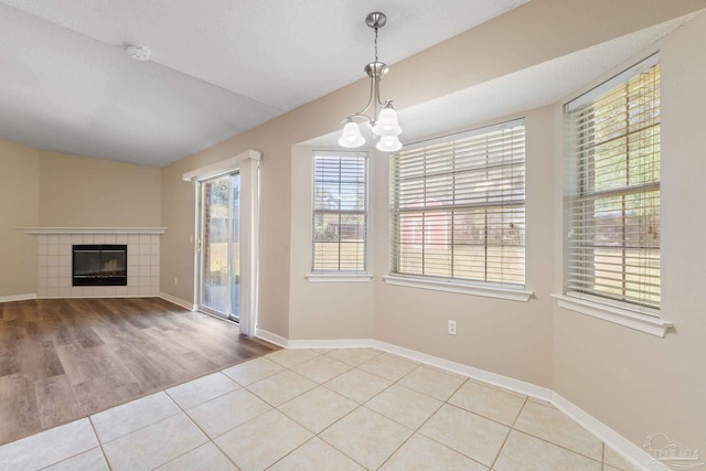 unfurnished dining area featuring light hardwood / wood-style flooring, a notable chandelier, a textured ceiling, and a tile fireplace