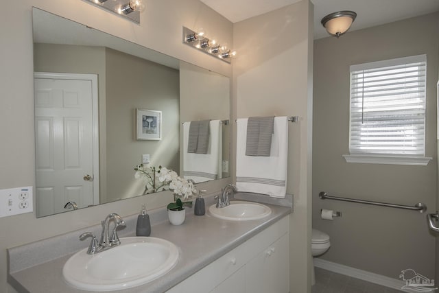 bathroom with double vanity, toilet, baseboards, and a sink