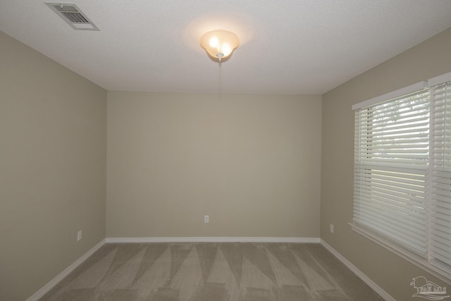 empty room featuring visible vents, light colored carpet, a textured ceiling, and baseboards