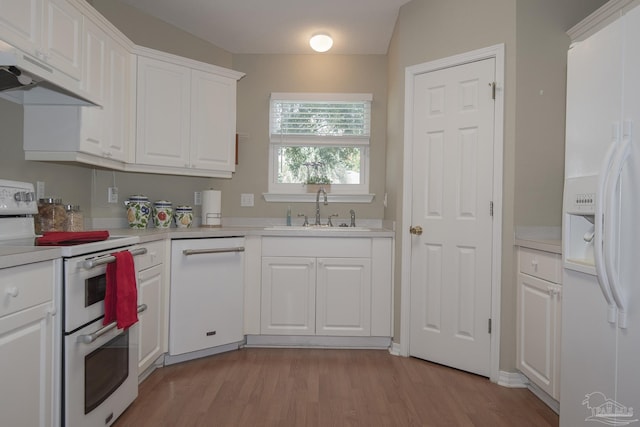 kitchen featuring white appliances, a sink, light countertops, under cabinet range hood, and white cabinetry