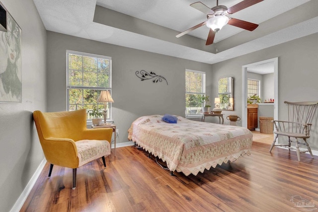 bedroom with a tray ceiling, hardwood / wood-style floors, and multiple windows