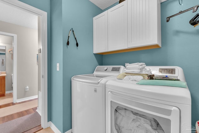 washroom featuring cabinets, a textured ceiling, washer and clothes dryer, and light hardwood / wood-style floors