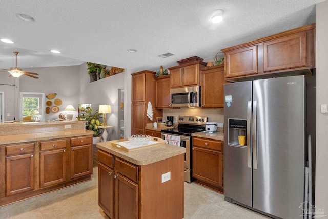 kitchen with a textured ceiling, stainless steel appliances, a center island, and ceiling fan