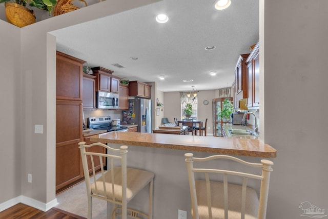 kitchen featuring sink, appliances with stainless steel finishes, a kitchen bar, kitchen peninsula, and light wood-type flooring