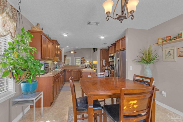 dining area with light tile patterned flooring, sink, vaulted ceiling, a textured ceiling, and ceiling fan with notable chandelier