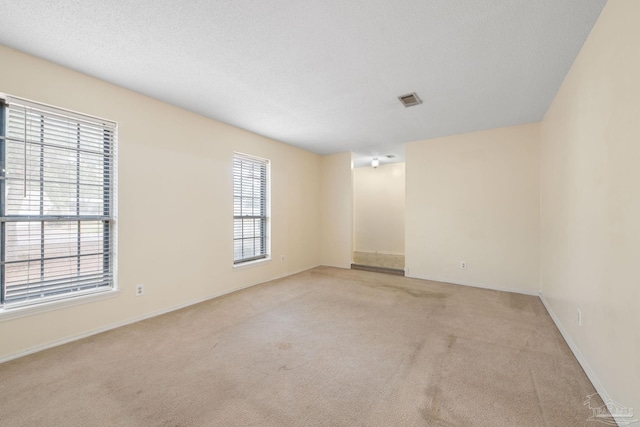 unfurnished room with light carpet, a textured ceiling, visible vents, and baseboards