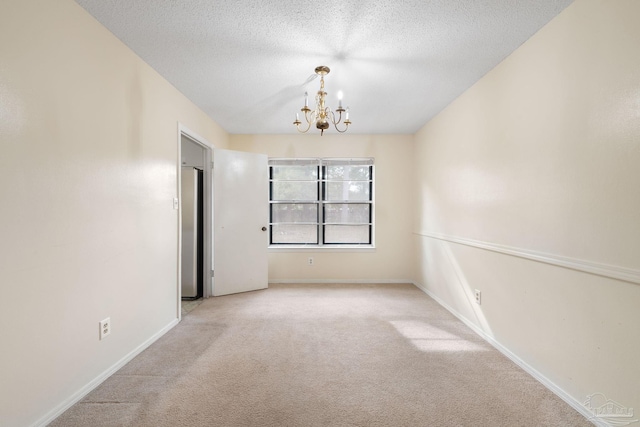 carpeted spare room with a chandelier, a textured ceiling, and baseboards