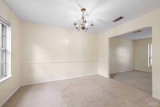 carpeted empty room with a chandelier, visible vents, a textured ceiling, and baseboards