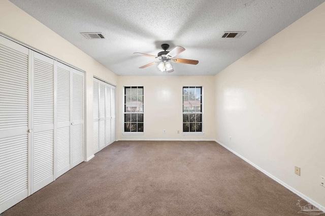 unfurnished bedroom featuring carpet floors, baseboards, visible vents, and two closets