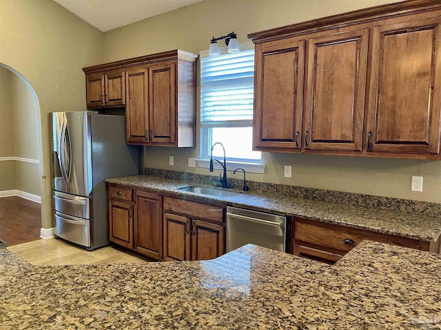 kitchen with dark stone counters, stainless steel appliances, baseboards, and a sink
