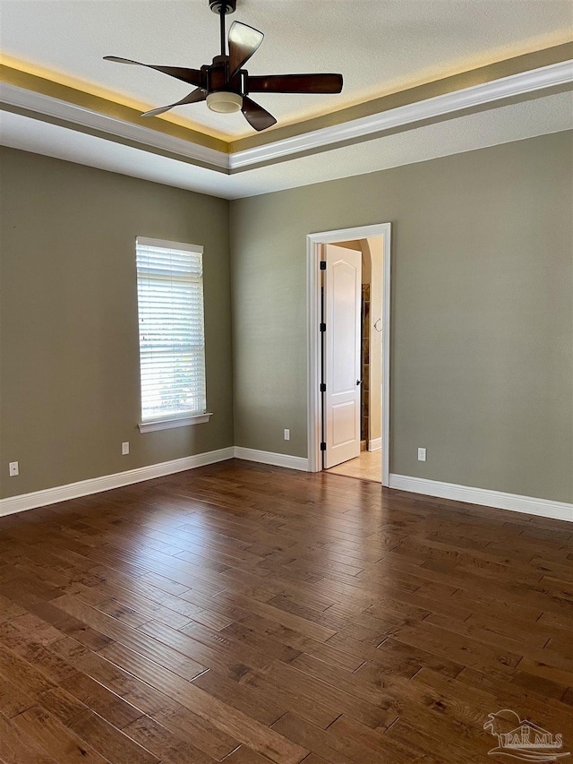 unfurnished room featuring dark wood finished floors, baseboards, a raised ceiling, and a ceiling fan