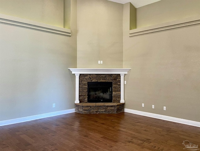 unfurnished living room featuring a high ceiling, a stone fireplace, baseboards, and dark wood-type flooring