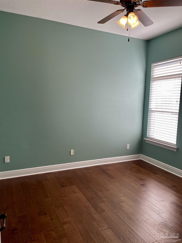 spare room with a ceiling fan, dark wood finished floors, and baseboards