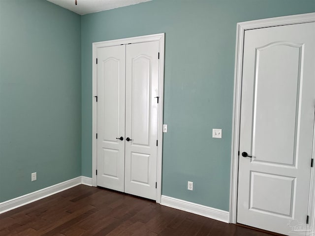 unfurnished bedroom with dark wood-style floors, a closet, and baseboards