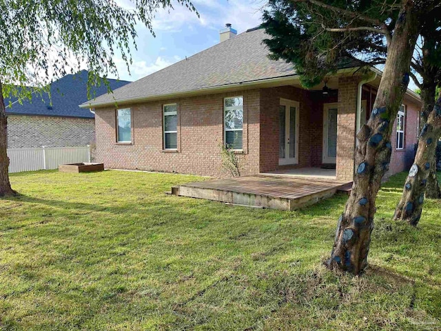 rear view of house featuring a chimney, brick siding, fence, a shingled roof, and a lawn